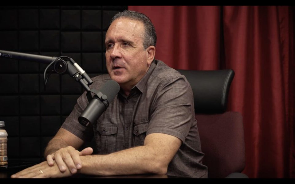man in gray shirt in podcast studio with red curtain behind him